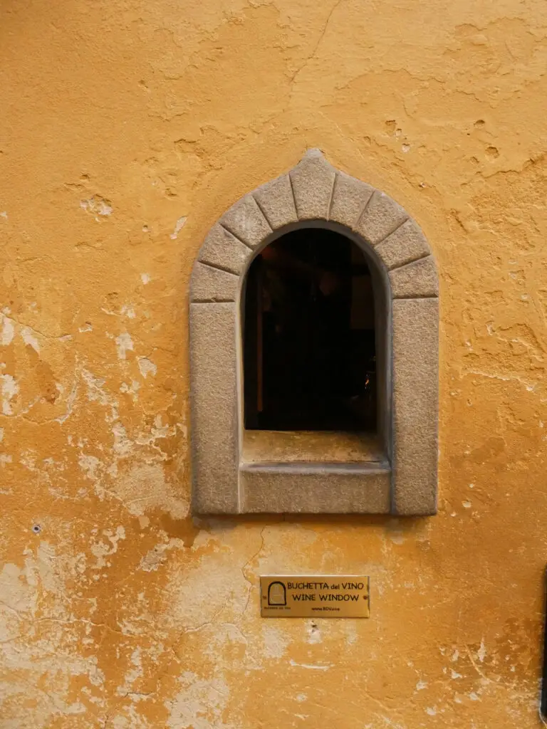 A tiny, arched wine window on a brightly colored wall, blending tradition with modern charm